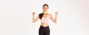 Fitness, sağlıklı yaşam tarzı ve refah konsepti. Gülümseyen Asyalı esmer spor kızı portresi aktif giyimli kadın atlet mezura, egzersiz yaparak kilo verme, beyaz arka plan..