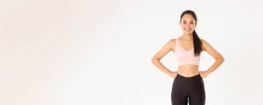 Spor, refah ve aktif yaşam tarzı konsepti. Neşeli ince ve güçlü Asyalı fitness kızı spor salonunda spor yapıyor, aktif giyimde elleri belinde duruyor, spor salonundaki iyi eğitimden sonra gülümsüyor..