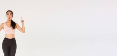 Afallamış ve etkilenmiş Asyalı kadın sporcu, spor giyimli kadın heyecanlı yüzüyle parmaklarını havaya kaldırıyor. Fitness kızı spor mağazasında özel bir teklifle merak etti..