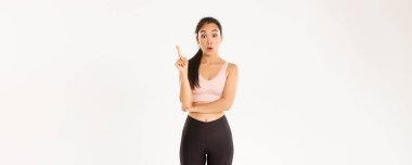 Spor, refah ve aktif yaşam tarzı konsepti. Düşünceli fit ve zayıf Asyalı kızın bir fikri var, sporcu kadın öneriler için işaret parmağını kaldır, egzersiz planı yap, beyaz arka planda dur.