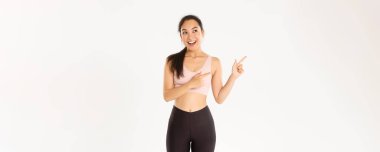 Spor, refah ve aktif yaşam tarzı konsepti. Heyecanlı, ince ve tatlı Asyalı fitness kızı, sol üst köşeyi gösteren bayan sporcu, spor malzemeleri satış promosyonu veya spor salonu teklifi gösteriyor.