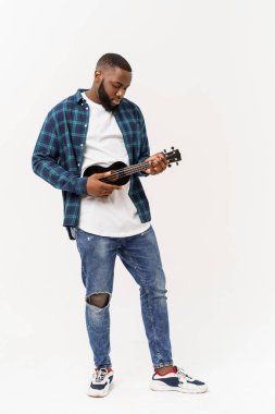 Genç ve yakışıklı Afro-Amerikan adam beyaz arka planda ukulele çalıyor.