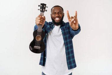 Genç ve yakışıklı Afro-Amerikan adam beyaz arka planda ukulele çalıyor.