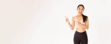 Spor, refah ve aktif yaşam tarzı konsepti. Heyecanlı, ince ve tatlı Asyalı fitness kızı, sol üst köşeyi gösteren bayan sporcu, spor malzemeleri satış promosyonu veya spor salonu teklifi gösteriyor.