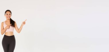 Gülümseyen, spor giyimli, zayıf Asyalı güzel bir kız, sağ üst köşeyi işaret ediyor, spor salonu üyeliği için davet ediyor, egzersiz teklifi sunuyor, fitness koçu sağlıklı diyet önerileri gösteriyor..