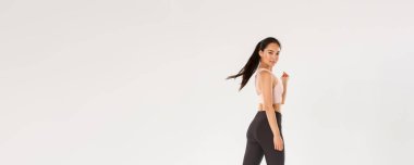 Şımarık, yakışıklı, spor yapan ince Asyalı kız, sporcu ya da antrenman koçu kendinden emin, motive olmuş bir ifadeyle yürüyen, kameraya dön lütfen gülümse, beyaz arka plan.