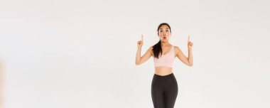 Afallamış ve etkilenmiş Asyalı kadın sporcu, spor giyimli kadın heyecanlı yüzüyle parmaklarını havaya kaldırıyor. Fitness kızı spor mağazasında özel bir teklifle merak etti..