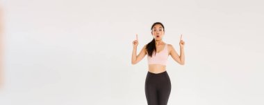 Spor, spor salonu ve sağlıklı vücut konsepti. Uzunluğu şaşırmış ve etkilenmiş Asyalı bayan sporcu, spor giyim dalında sporcu kadın vay canına diyor ve parmaklarını havaya kaldırıyor, spor malzemeleri için harika indirimler gösteriyor..