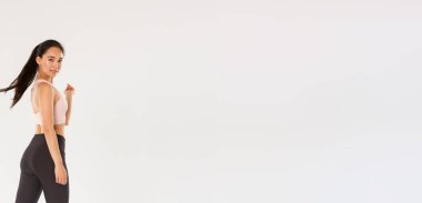 Şımarık, yakışıklı, spor yapan ince Asyalı kız, sporcu ya da antrenman koçu kendinden emin, motive olmuş bir ifadeyle yürüyen, kameraya dön lütfen gülümse, beyaz arka plan.