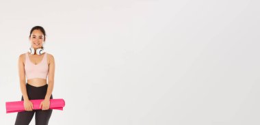 Spor salonunda antrenman için antrenman yaparken kameraya bakan lastik minderli, kulaklıklı, gülümseyen ince Asyalı kız..