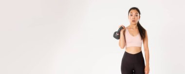 Spor, refah ve aktif yaşam tarzı konsepti. Yakışıklı esmer Asyalı fitness kızı portresi, spor salonunda vücut geliştirme kursuna kaydolma, kettlebell ağırlığı, beyaz arka planda dikilme,.