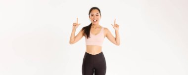 Spor, refah ve aktif yaşam tarzı konsepti. Gülümseyen enerjik Asyalı fitness kızı, etkinliğe davet edilen bayan sporcu, egzersiz vitesi reklamını gösteren, parmaklarını havaya kaldıran, logo pankartın..