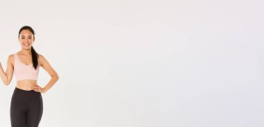 Spor, spor salonu ve sağlıklı vücut konsepti. Gülümseyen güzel Asyalı fitness kızı, aktif giyimli bayan sporcu sol eli gösteren giyim koçu eğitim ekipmanları, beyaz arka plan..