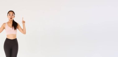 Spor, spor salonu ve sağlıklı vücut konsepti. Uzunluğu şaşırmış ve etkilenmiş Asyalı bayan sporcu, spor giyim dalında sporcu kadın vay canına diyor ve parmaklarını havaya kaldırıyor, spor malzemeleri için harika indirimler gösteriyor..