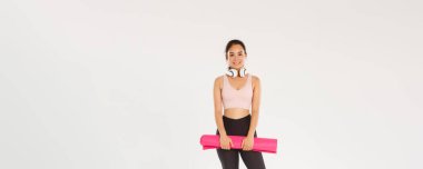 Spor salonunda antrenman için antrenman yaparken kameraya bakan lastik minderli, kulaklıklı, gülümseyen ince Asyalı kız..