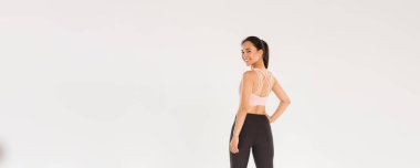 Tam boy gülümseyen ince ve güçlü kadın fitness koçu, spor giyim dalında bayan sporcu arkana dön ve kameraya mutlu, motive olmuş bir ifadeyle bak, çalışmaya hazır bir kız, beyaz bir arka plan..