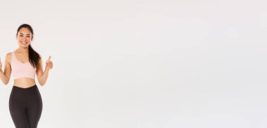 Tatmin olmuş gülümseyen, yakışıklı Asyalı fitness kızı, aktif giyinen sporcu kadın başparmak kaldıran ve gülümseyen, gururlu bayan sporcu günlük çalışma hedefi, beyaz arka plan.