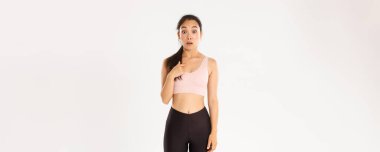 Spor, refah ve aktif yaşam tarzı konsepti. Spor kıyafetleri içinde şaşırmış Asyalı bir kız şaşkın şaşkın, seçilmiş ya da seçilmiş, beyaz bir arka plan.