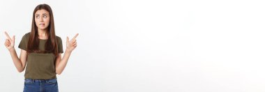 Gri arka planda yalnız duran mutlu ve şaşırmış genç bir bayan portresi. Kamera işaret ediyor