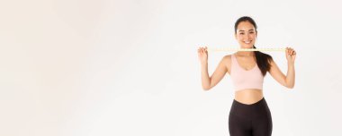 Fitness, sağlıklı yaşam tarzı ve refah konsepti. Gülümseyen Asyalı esmer spor kızı portresi aktif giyimli kadın atlet mezura, egzersiz yaparak kilo verme, beyaz arka plan..
