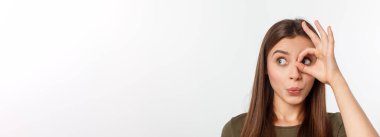 Neşeli, şirin, şık, çekici, trend bir kızın, parmaklarıyla dürbün yapan, gri arka planda izole edilmiş, keyifli bir kız portresi..