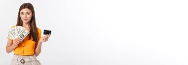 Gri arka planda tek başına duran mutlu genç bir kadının fotoğrafı. Para ve kredi kartını bir kenara bırakarak.