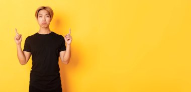 Surat asan asyalı adamın portresi hayal kırıklığına uğramış, parmaklarını havaya kaldırmış, sarı arka plan..