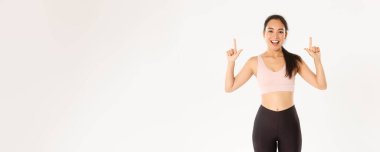 Spor, refah ve aktif yaşam tarzı konsepti. Gülümseyen enerjik Asyalı fitness kızı, etkinliğe davet edilen bayan sporcu, egzersiz vitesi reklamını gösteren, parmaklarını havaya kaldıran, logo pankartın..