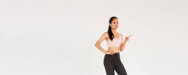 Spor, spor salonu ve sağlıklı vücut konsepti. Şüpheci ve hoşnutsuz bayan sporcu Asyalı sporcu somurtuyor ve somurtuyor, hayal kırıklığına uğruyor, sol üst köşeyi işaret ediyor ve şikayet ediyor..