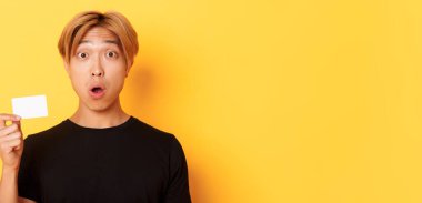 Sarı saçlı, şaşırmış ve şaşırmış görünen, sarı arka planda duran Asyalı adamı yakından çek..