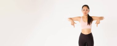 Spor, refah ve aktif yaşam tarzı konsepti. Surat asan ve hayal kırıklığına uğramış Asyalı antrenman kızı, aktif giysili bayan sporcu üzgün, kötü bir şeye işaret eden ve ona tepeden bakan, beyaz arka plan.