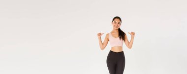 Tam boy profesyonel fitness koçu, kendini gösteren Asyalı kız sporcu, mutlu gülümseyen, spor salonunda antrenman yapan, spor giyim kuşamları giyen, beyaz arka plan giyen....