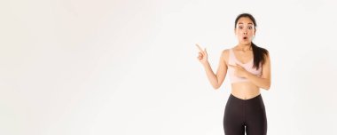 Spor, refah ve aktif yaşam tarzı konsepti. Etkilenmiş ve heyecanlı sporcu, aktif giyimli Asyalı sporcu ağzı açık geziyor ve sol üst köşesini logo afişinize işaret ediyor..