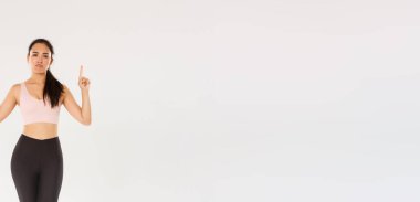 Spor, spor salonu ve sağlıklı vücut konsepti. Eğlendirilmemiş ve şüpheci fitness kızı, spor giyim sektöründe Asyalı bayan sporcu şikayetçi, küskün, hoşnutsuz ve parmakla işaret eden beyaz arka plan.