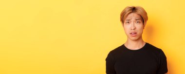 Kafası karışmış, kafası karışmış, kafası karışmış, ağzı açık, suratı asık, sarı arka planda duran Asyalı sarışının yakın çekimi..