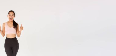 Şaşırmış ve tatmin olmuş bir şekilde gülümseyen fitness kızı, aktif giyinen bayan sporcu yeni spor salonunu ya da egzersiz programını seviyor, baş parmaklarını gösteriyor, antrenmanlara başlamaya teşvik ediyor ya da egzersiz yapıyor..