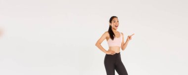 Spor, spor salonu ve sağlıklı vücut konsepti. Sporcu ve taytlı heyecanlı Asyalı bayan sporcular sol üst köşeyi gösterip bakıyorlar. Heyecanlı bir şekilde spor aletleri için uygun fiyatlar buldular..