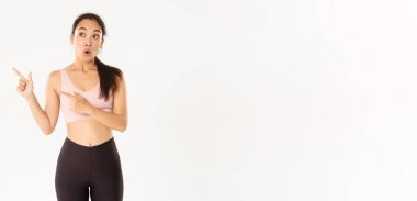 Spor, refah ve aktif yaşam tarzı konsepti. Etkilenmiş ve heyecanlı sporcu, aktif giyimli Asyalı sporcu ağzı açık geziyor ve sol üst köşesini logo afişinize işaret ediyor..