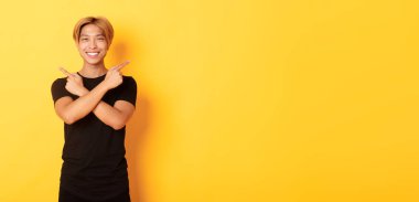 Yakışıklı, kararlı, sarışın Asyalı bir adamın portresi. Öğrenci iki farklı türü gösteriyor. Sarı arka planda duruyor..