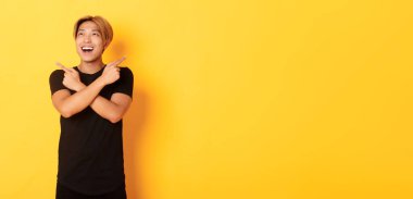 Mutlu gülümseyen sarı saçlı Asyalı adam portresi solda, iki farklı yöne bakıyor, sarı arkaplan..