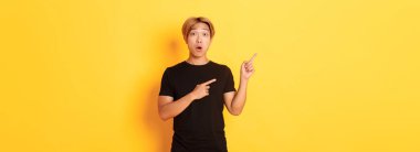 Siyah tişörtlü, etkilenmiş ve heyecanlı Asyalı adamın portresi, logonuza tepki verin, sol üst köşeyi işaret ederek..