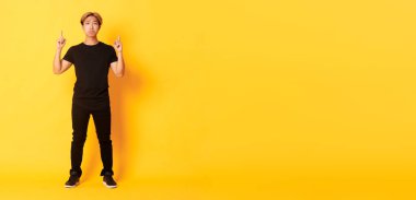 Uzun boylu, üzgün, yakışıklı, sarı saçlı, suratını ekşiten, pişmanlık gösteren, sarı arka planda duran, üzgün, yakışıklı Koreli bir adam..