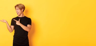 Yakışıklı, gülümseyen Asyalı bir adamın portresi. Elinde bir şey tutuyor ve onu işaret ediyor. Sarı arka planda duruyor..