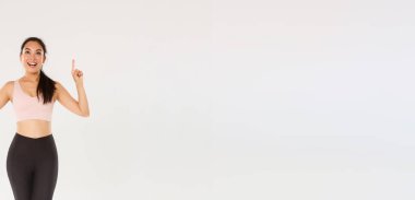 Spor, spor salonu ve sağlıklı vücut konsepti. Spor kıyafetli, heyecanlı, gülümseyen kadın sporcu hayrete düşmüş ve parmaklarını havaya kaldırmış, spor salonunun keyfini çıkaran bayan sporcu, yeni üyeleri davet et..