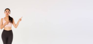 Şüpheci, hayal kırıklığına uğramış Asyalı fitness kızı, sporcu kadın sırıtarak ve somurtarak kötü spor salonundan ya da berbat spor aletlerinden şikayet ederken, sağ üst köşeden memnuniyetsiz, beyaz arka plan.