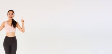 Spor, spor salonu ve sağlıklı vücut konsepti. Neşeli, gülümseyen Asyalı fitness kızı, spor giyimli bayan sporcu reklamı gösteren, parmaklarını havaya kaldıran ve antrenman için davet eden,.