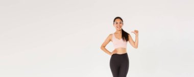 Spor ve bacaklı, kendinden emin gülümseyen Asyalı bayan sporcu, kendini gösteren fitness kızı, aktif ve sağlıklı bir yaşam tarzı, profesyonel olmak, beyaz arka planda durmak..