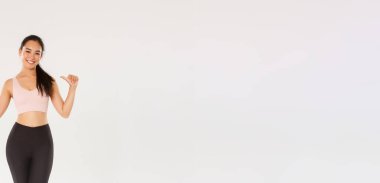 Tam boy profesyonel fitness koçu, kendini gösteren Asyalı kız sporcu, mutlu gülümseyen, spor salonunda antrenman yapan, spor giyim kuşamları giyen, beyaz arka plan giyen....