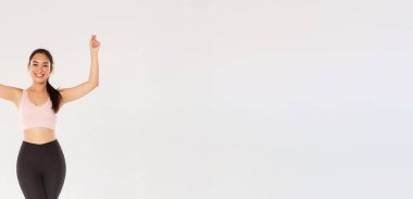 Sıska ve sağlıklı Asyalı kız egzersizleri spor kıyafetleri içinde el kaldırarak işaret ya da afiş tutar gibi spor malzemesi ya da spor salonu üyeliği indirimi gibi el kaldırıyor..