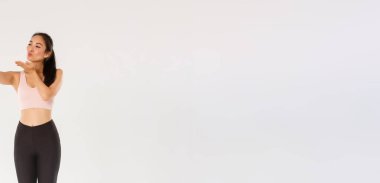 Spor kıyafetleri giyip spor salonundan selfie çeken ya da spor salonundan canlı yayın yapan, cep telefonu ekranına hava öpücüğü gönderen, beyaz arka planda duran, spor salonundaki sevimli ve aptal kadın blogcu..